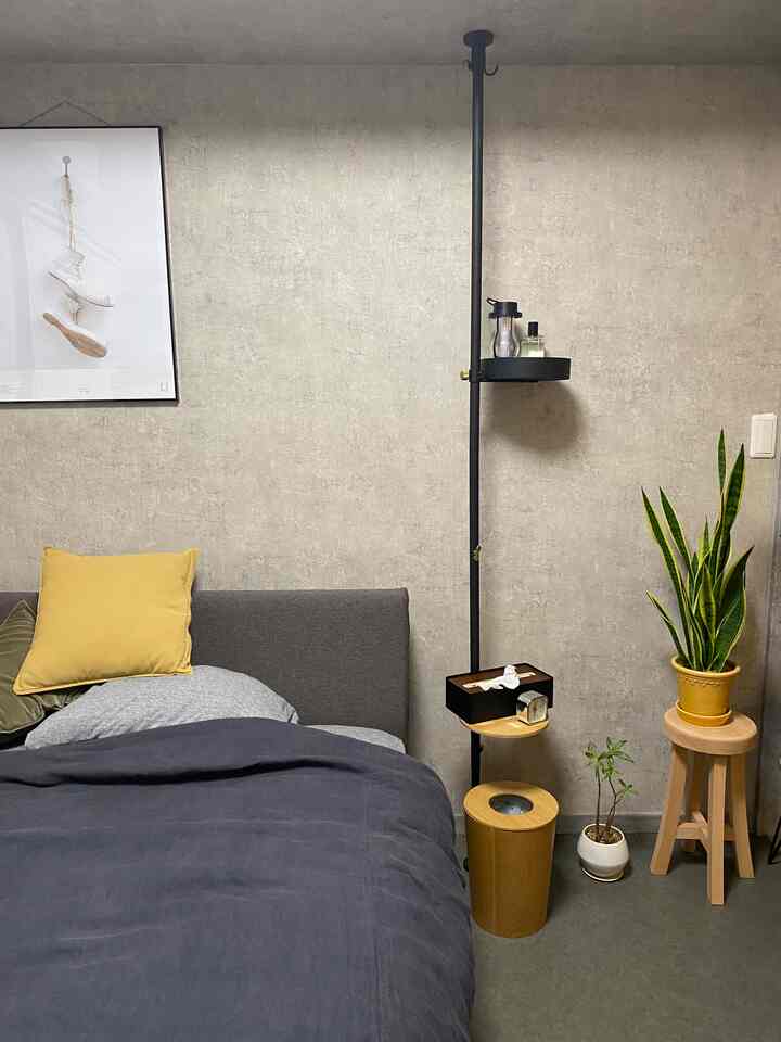 グレーとナチュラルカラーの寝室、ベッドとクッション、縦型ポール棚が配置された落ち着いたインテリア