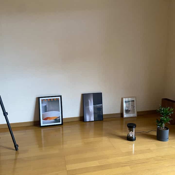 温かみのある木目調の床と白い壁が特徴の玄関空間、床に三枚のポスターと小さな観葉植物が置かれたミニマルなインテリア