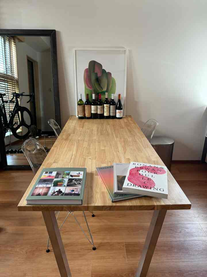 Natural wood tone studio apartment featuring a long desk with art books and wine bottles in a simple interior