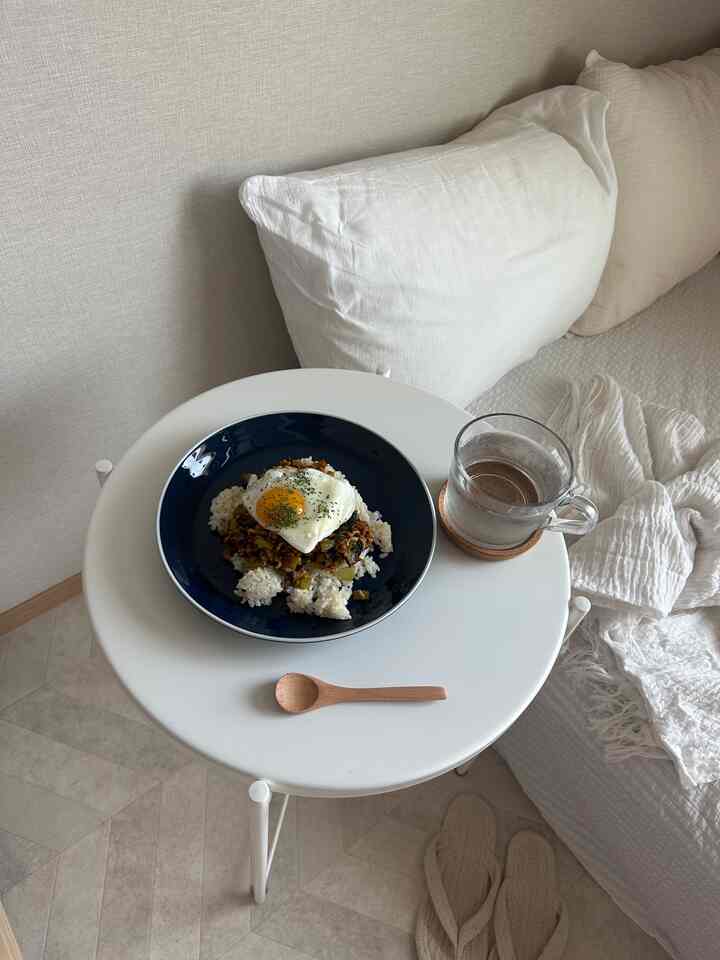 白を基調としたワンルーム寝室、白いサイドテーブルに食事とマグカップが配置された雰囲気のある空間