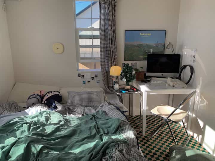 Bedroom with white walls and green checkered carpet featuring bed and desk, creating a cozy retro atmosphere
