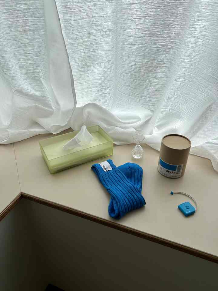 明るいホワイトカーテンとベージュのテーブルの上に青い靴下とティッシュケースが置かれたミニマルな空間