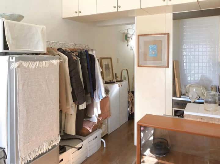 ナチュラルカラーの狭いワンルーム、洋服ラックと収納が配置された落ち着いた整然としたインテリア
