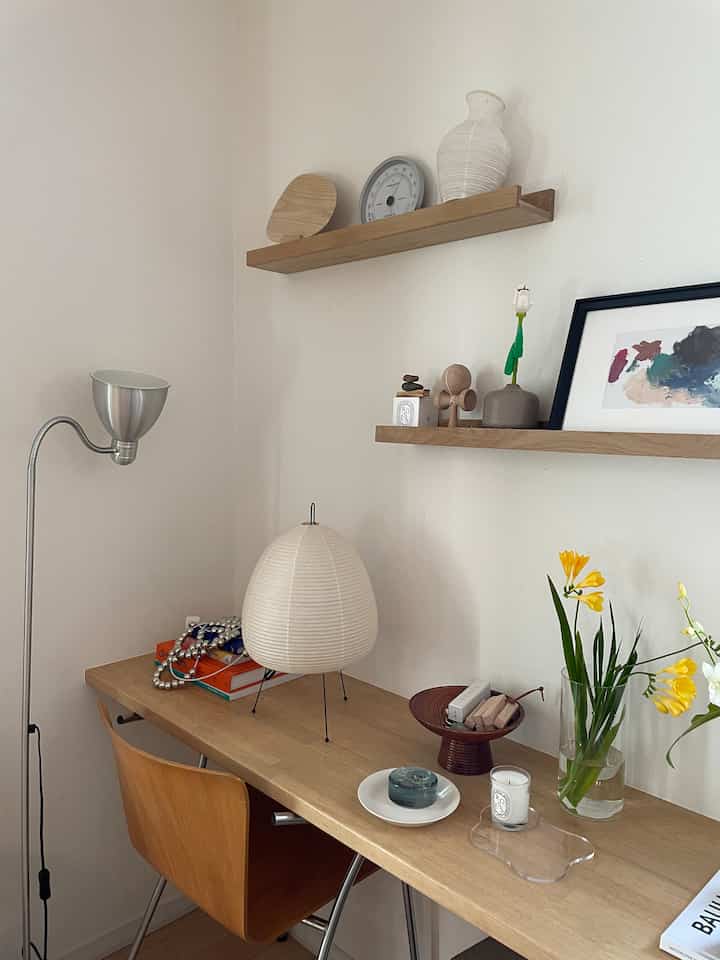 清潔な白い壁とナチュラルな木製のデスクと棚が調和したシンプルなホームオフィス、花瓶や時計、額縁が配置された雰囲気のあるインテリア