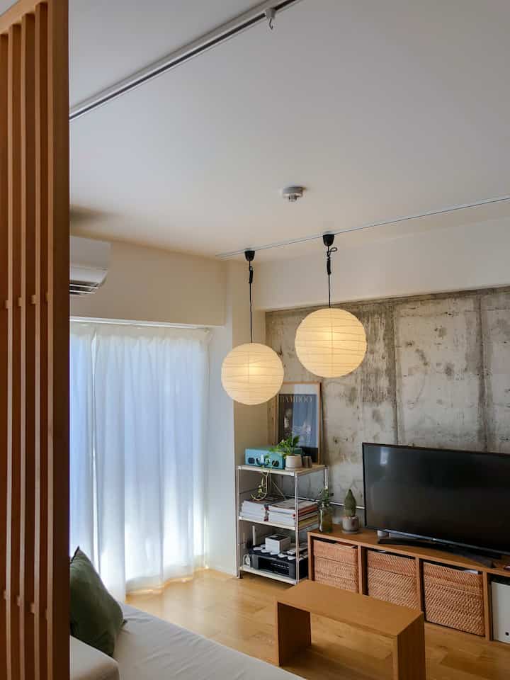 ナチュラルな木目調と白が調和するリビング、ラタンバスケットとペンダントライトが映えるシンプルな空間