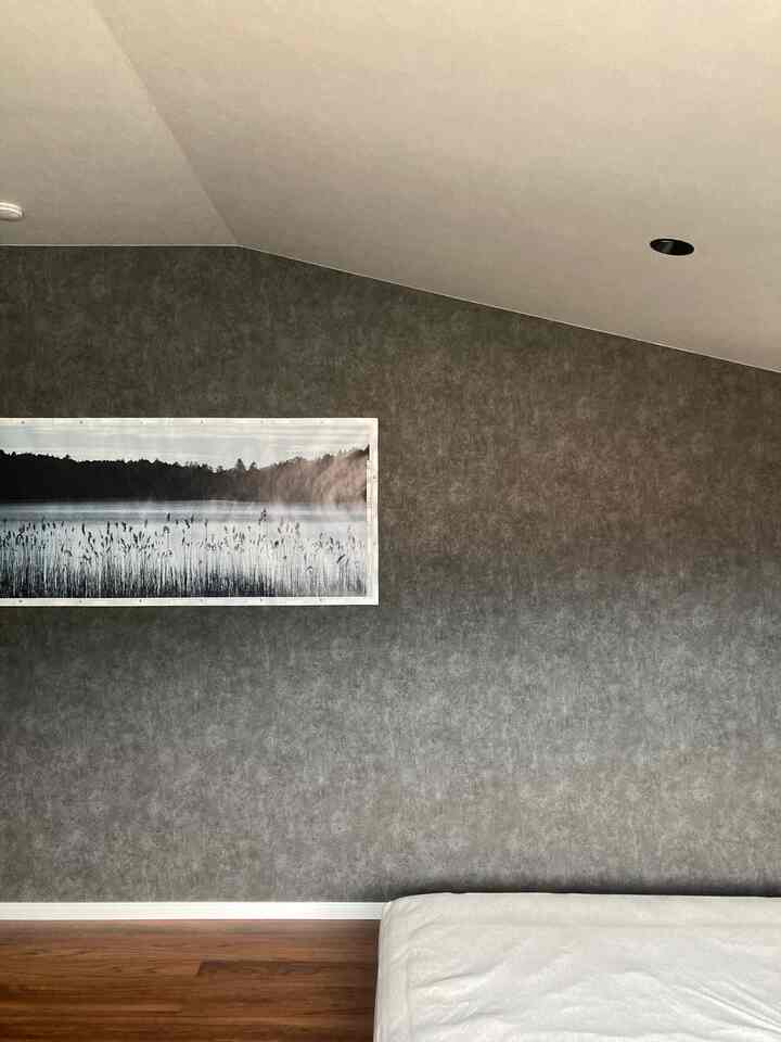 ダークグレーの壁と木目調の床があるミニマルな寝室、白いベッドマットレスが配置された空間