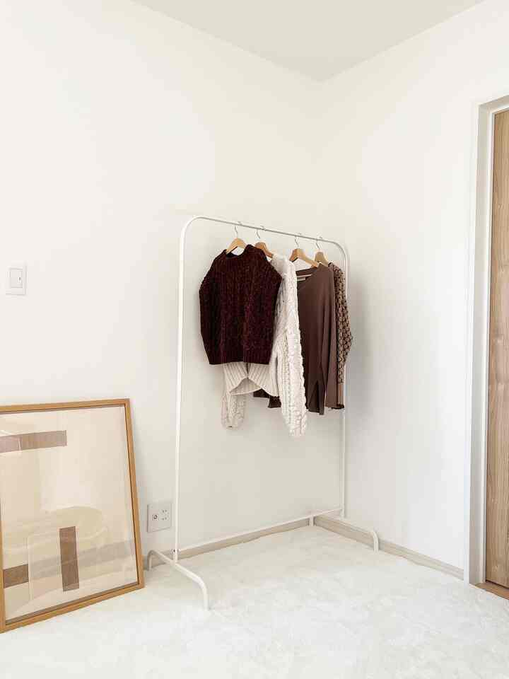 白とナチュラルカラーのミニマルな寝室、中央に白いメタルのハンガーラックと柔らかい白いラグが敷かれた空間