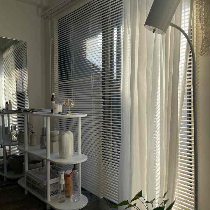 白を基調としたベランダ、ブラインドとカーテンが配置されて柔らかな採光が差し込む清潔感のある空間