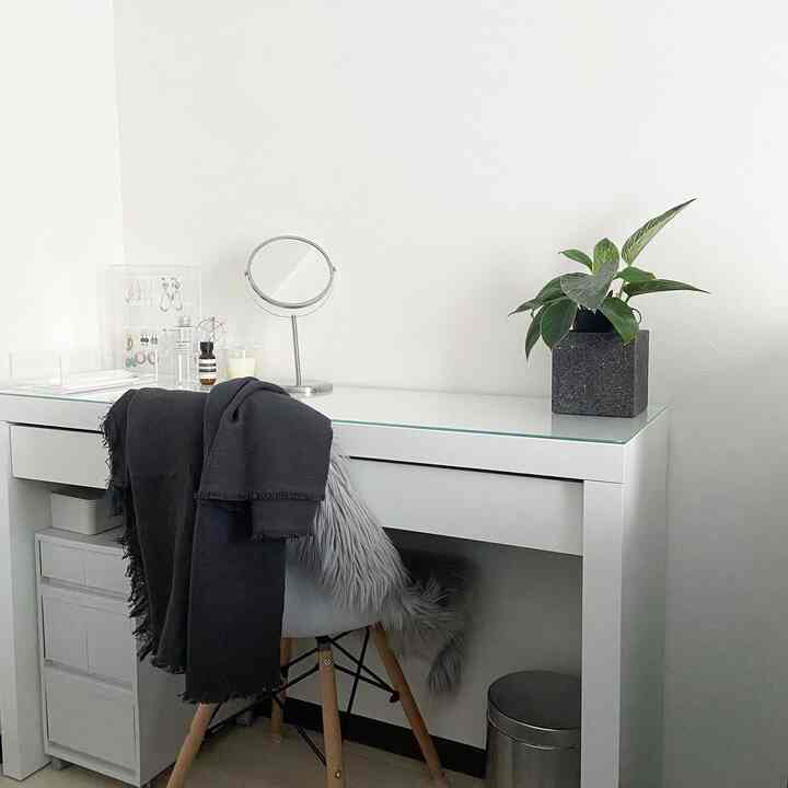 White-toned dressing room featuring a minimal vanity with gray blanket and a plant, creating a clean atmosphere