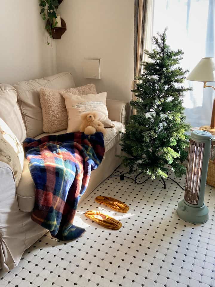 白とナチュラルカラーのコンパクトなリビング、ベージュのソファとレトロなカーボンヒーターが配置された雰囲気のあるインテリア