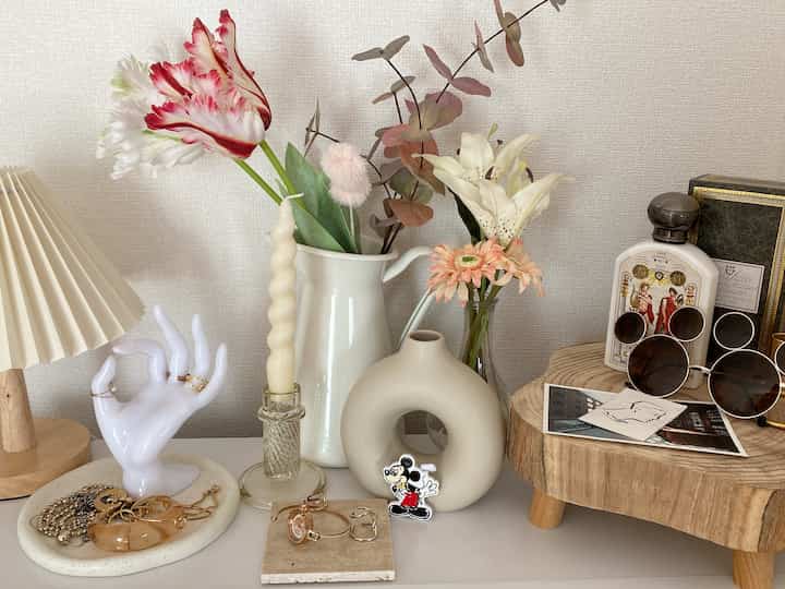 白とベージュの色調の小さなテーブルスペース、手の形のアクセサリースタンドや花瓶、ムードランプが配置されたシンプルでナチュラルなインテリア