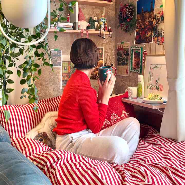 Red and white toned bedroom space with Christmas decorations, a person in red holding a mug creating a cozy atmosphere