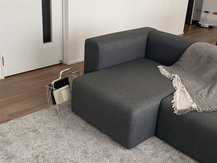 ダークグレーのソファとアイアン製マガジンラックが配置されたシンプルで落ち着いたリビング、無印良品のスロー付き