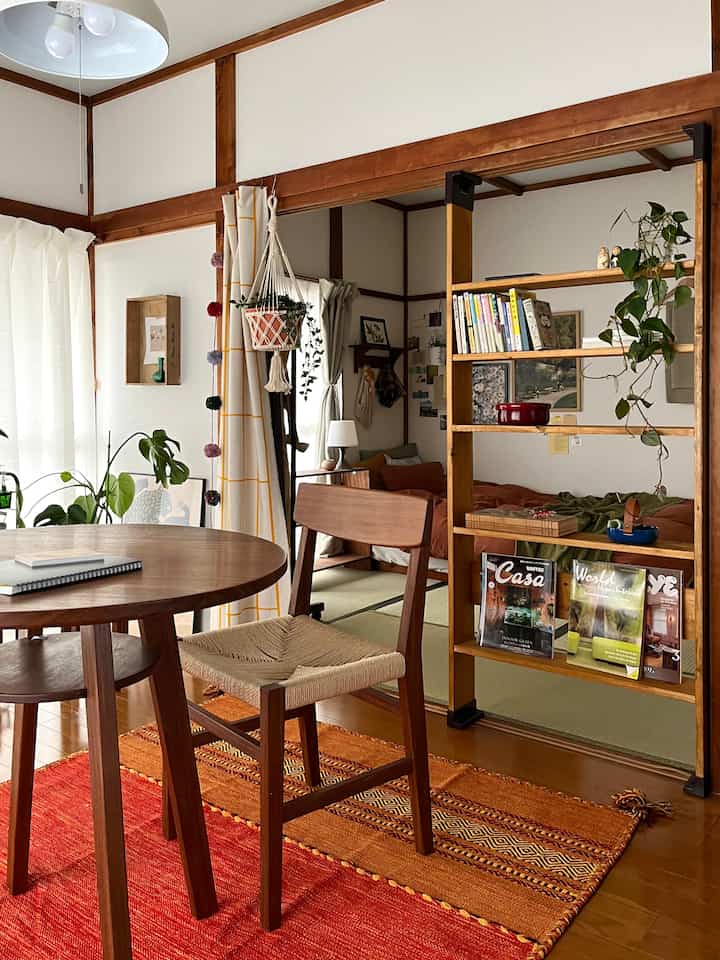 ブラウンの木目調と赤いキリムラグが調和したワンルームのリビング、植物と本棚が配置された自然な雰囲気のインテリア