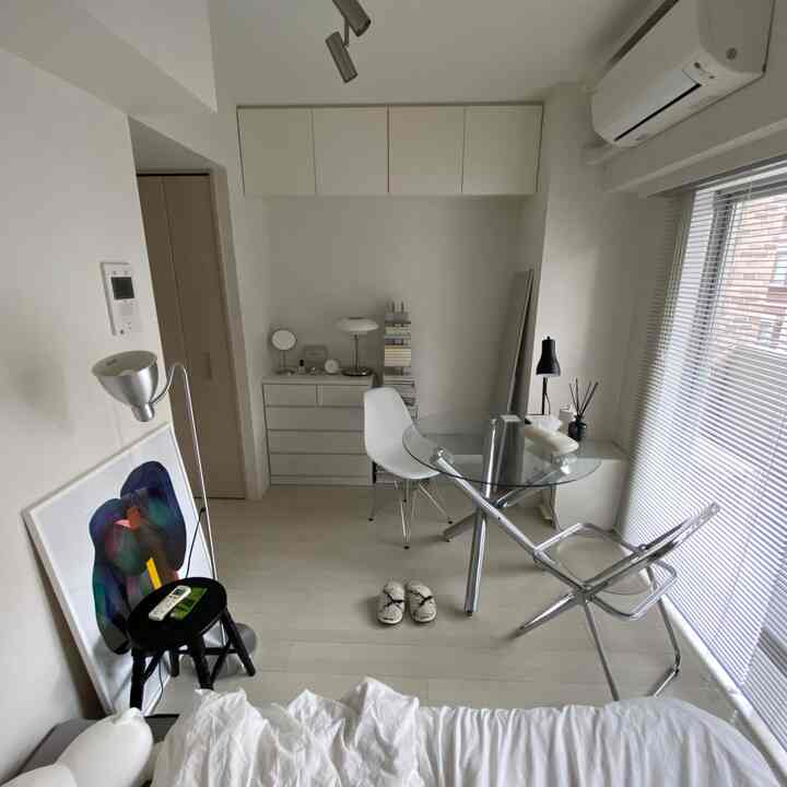 白とナチュラルトーンのワンルーム寝室、透明なガラステーブルと白いダイニングチェアが配置されたシンプルでコンパクトな空間