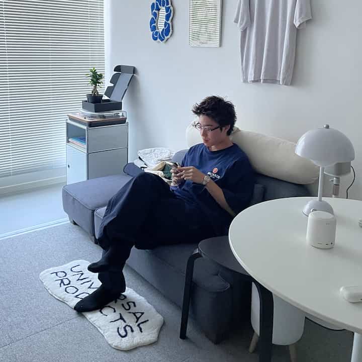 White and gray toned living room featuring a simple gray sofa with a young man sitting comfortably using his phone