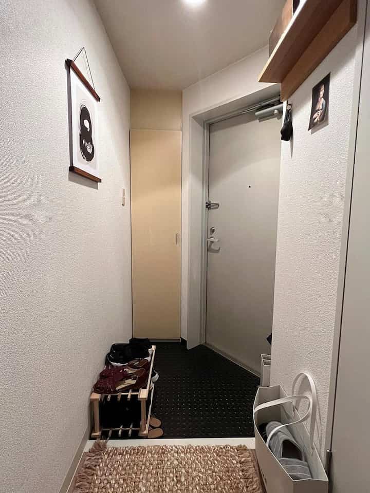 白い壁とナチュラルな木製の靴ラックと壁掛け棚が配置された狭い玄関の印象的なインテリア