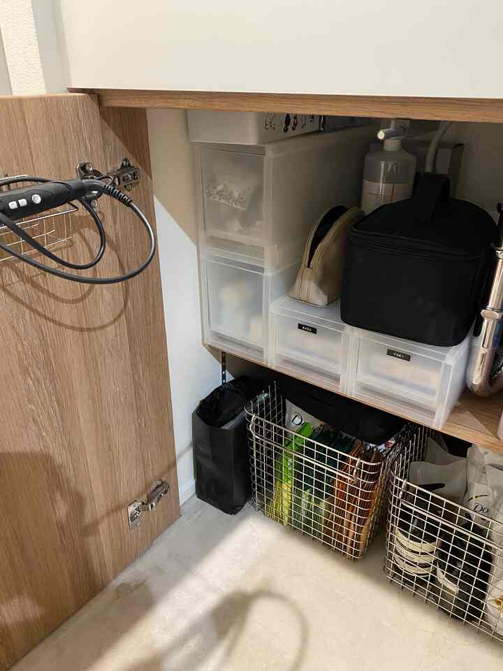 白と茶色のトーンのバスルーム収納スペース、透明なポリプロピレンケースとステンレスワイヤーバスケットが整頓されている印象的な空間