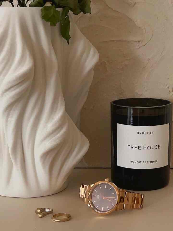 白い彫刻のような花瓶と黒いキャンドル、ゴールドの時計と指輪が並ぶシンプルなインテリア