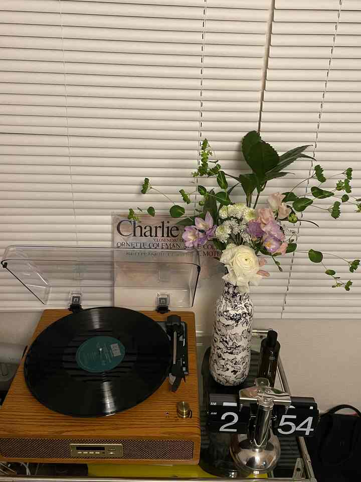 木目調と白いブラインドが調和する空間、レトロなレコードプレーヤーと花瓶が置かれた雰囲気のあるコーナー