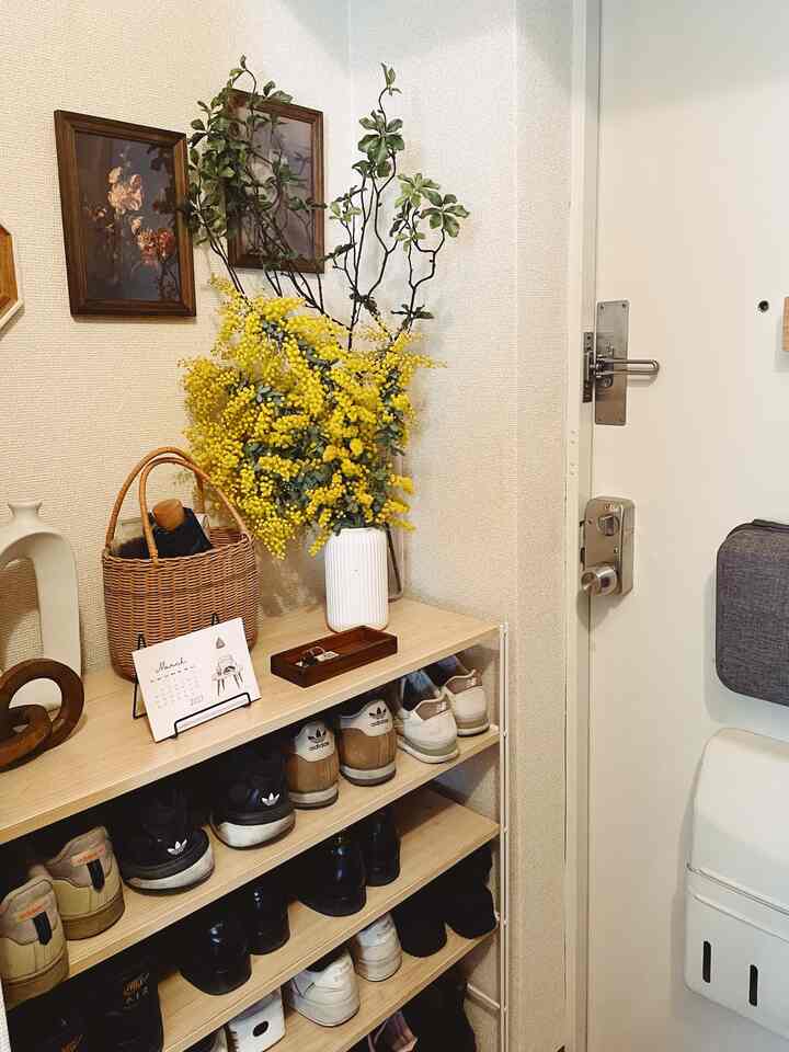 明るいナチュラルカラーの玄関、シューズラックと黄色いミモザの花瓶が配置されたシンプルで温かみのあるインテリア