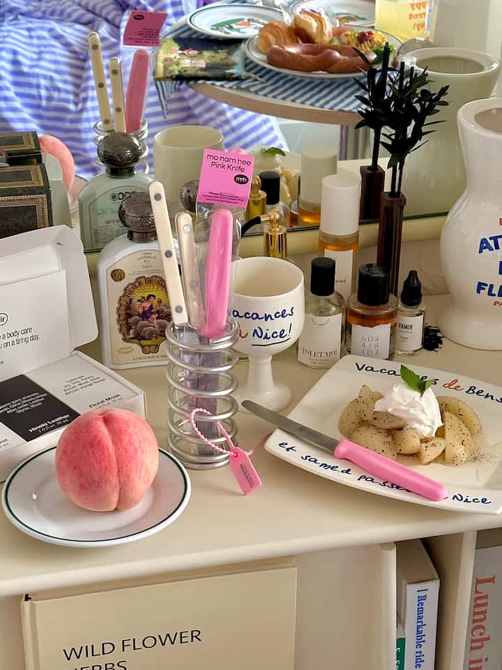 白とピンクの調和が取れたシンプルなキッチン空間、カトラリースタンドや果物、皿が置かれた落ち着いた雰囲気のテーブル