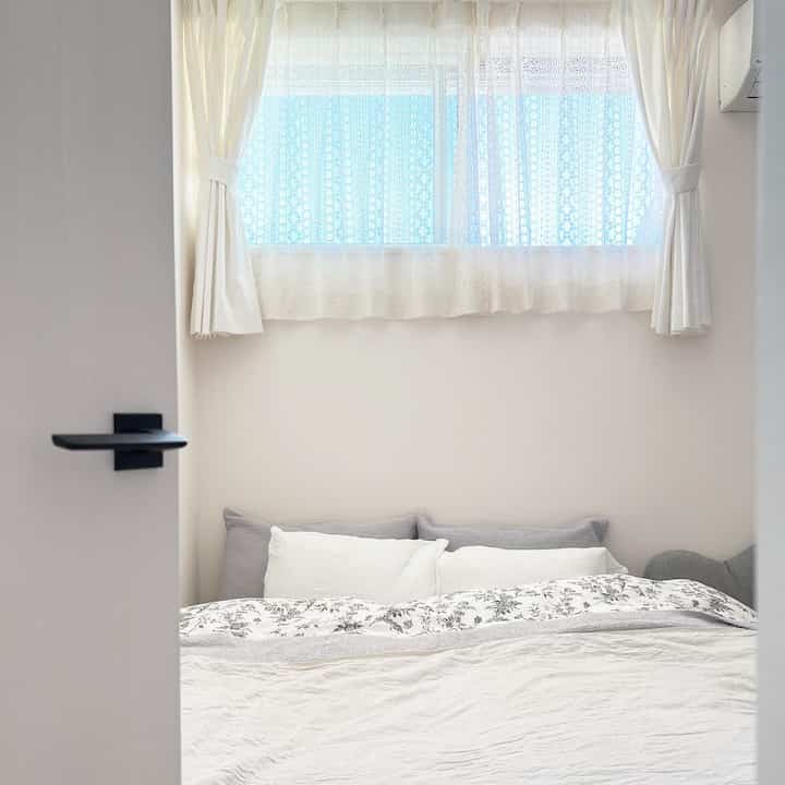 白とグレーのトーンの子供部屋兼寝室、カーテンとクイーンサイズマットレスが配置された落ち着いた雰囲気のインテリア