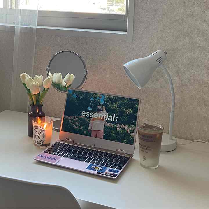 白を基調としたホームオフィスのワークスペース、机の上にノートパソコンとキャンドル、テーブルランプが置かれた印象的な空間