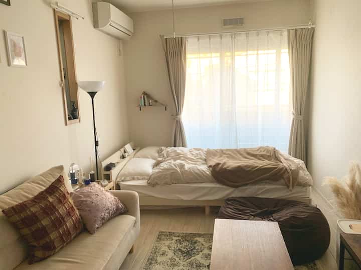 ベージュとブラウンの色調のワンルーム寝室、ソファとフロアランプが配置された落ち着いた雰囲気のインテリア