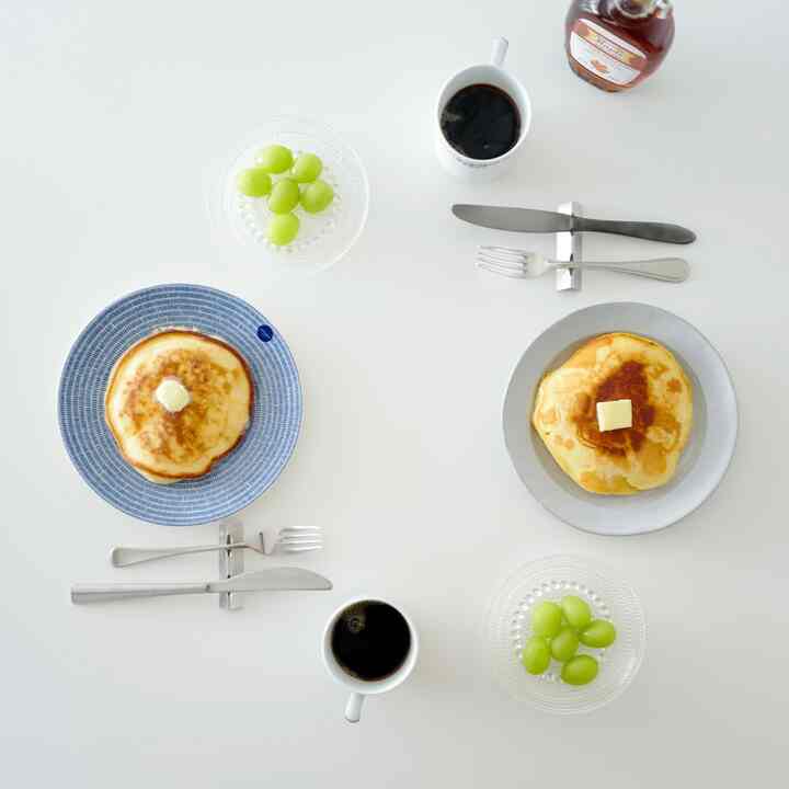 白を基調としたダイニングテーブルに北欧風の皿と透明なガラスボウル、マグカップが配置された清潔感のある食事空間