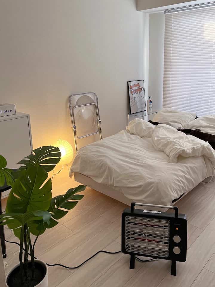 白を基調とした寝室、電気ストーブと掛け布団カバーが配置されたモダンでナチュラルな雰囲気のある空間