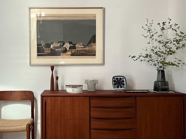 白い壁と木目調のサイドボード、花瓶と額縁が配置された北欧風の雰囲気あるリビングインテリア