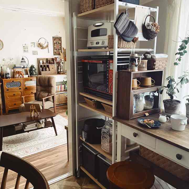 Natural tone kitchen connected to living room, featuring wooden furniture and storage shelves creating a cozy space