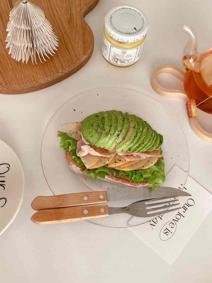 ベージュトーンのテーブルにアボカドのオープンサンドとティーポットが置かれた雰囲気のあるおうちカフェ