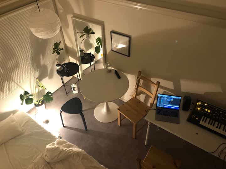 White and natural toned studio apartment featuring a central round dining table and a work desk on the right, creating a cozy space