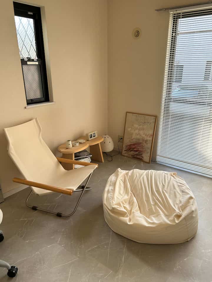 明るいベージュ色調のコンパクトなくつろぎスペース、ナチュラルなアームチェアとビーンバッグ、サイドテーブルが配置された落ち着いた雰囲気のインテリア