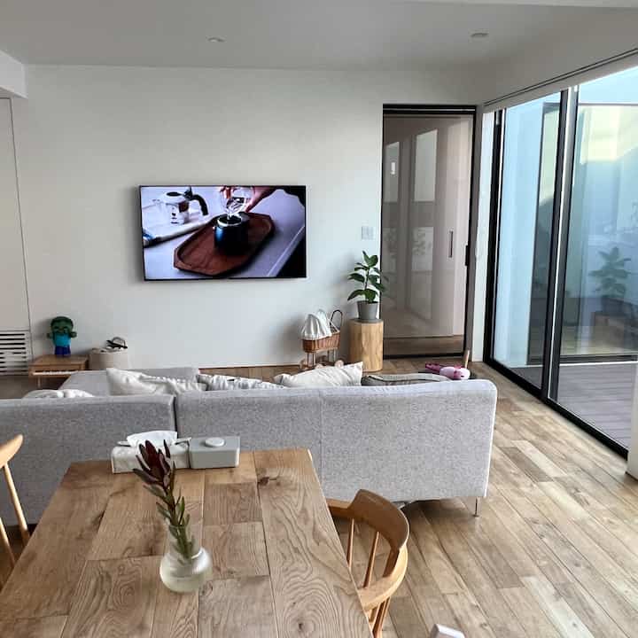 白い壁と木目調の床、グレーのソファと木製ダイニングテーブルがあるリビング、子供のおもちゃが見える自然でモダンな雰囲気のインテリア