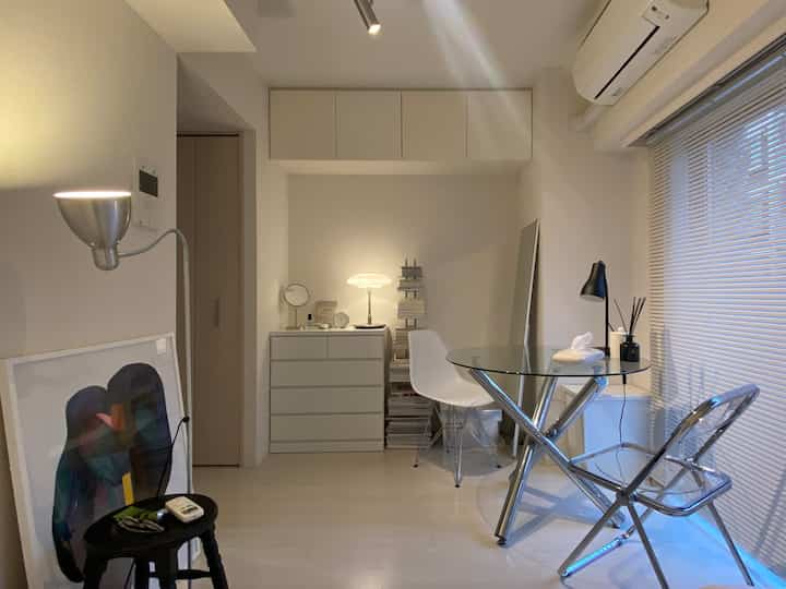 Small living room in white and silver tones featuring blinds and glass table chairs with a minimal style