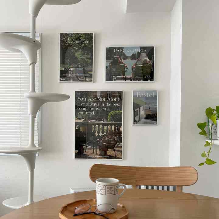 白と木目調のリビング、壁にポスターが掛かり、テーブル上にコーヒーカップとメガネが置かれた印象的なホームカフェ空間