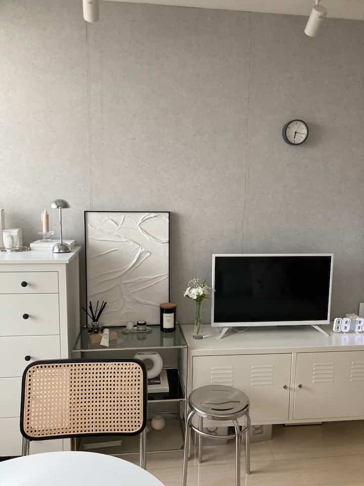Bright white and gray toned living room featuring stainless steel stool and rattan chair in a modern clean space