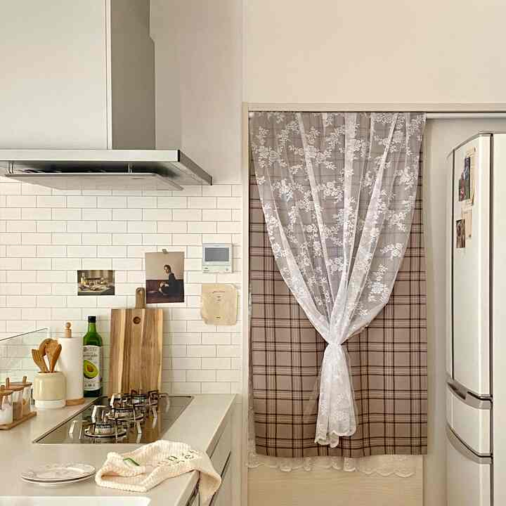 ナチュラルな色調のキッチン空間、レースのカーテンと木製調理器具が温かみのある雰囲気を演出するインテリア