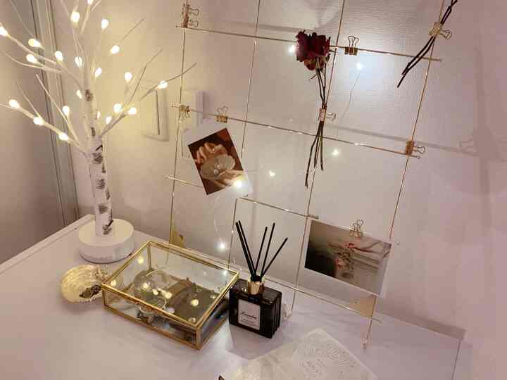 Cozy desk corner in warm gold and white tones, featuring string lights and a gold wire photo frame with clipped pictures