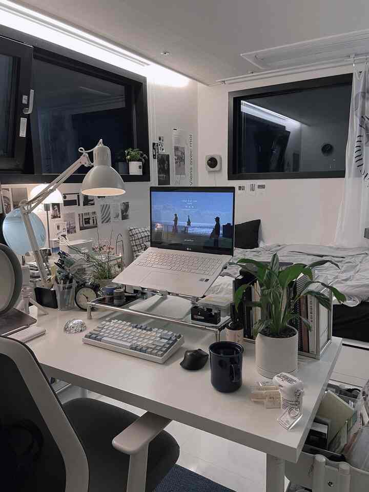 White-toned home office featuring a desk with laptop, keyboard, clock, and plant in a cozy workspace