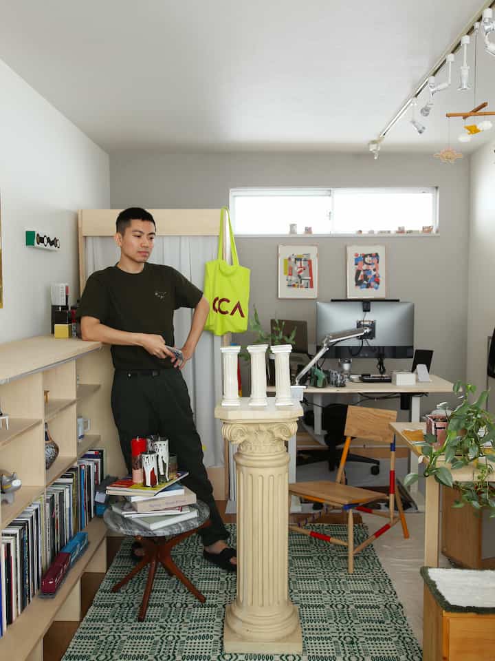 Beige and natural tone studio apartment featuring Greek-style column objet at center, with desk, plants, and bookshelf creating a modern interior