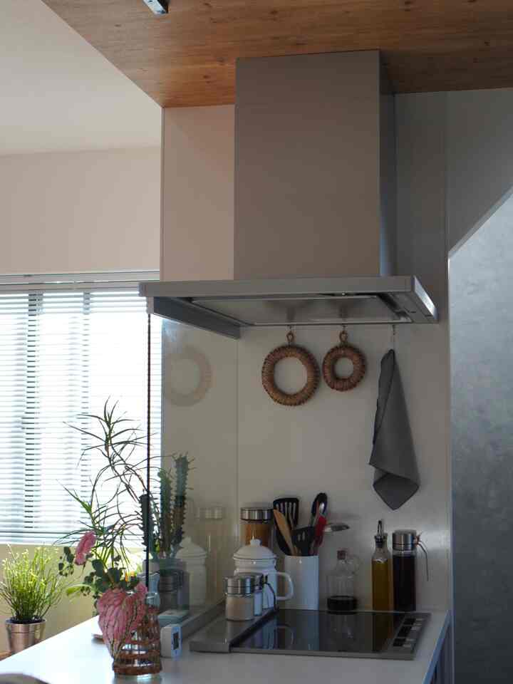 ナチュラルな色調のキッチン、木目調の天井と植物、整頓された調理器具とスパイスジャーが配置された清潔感のある空間