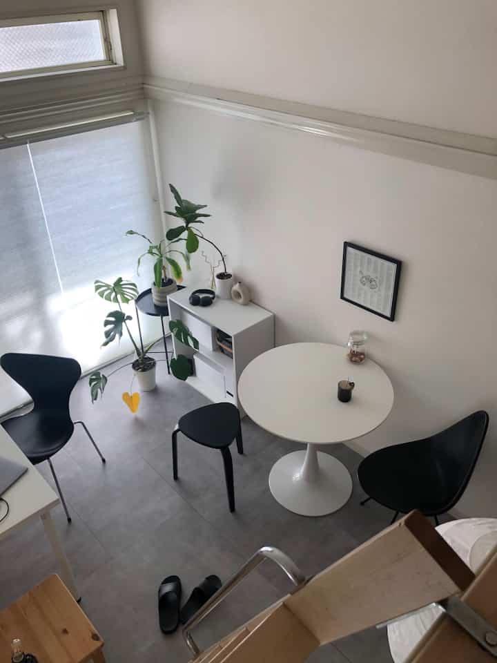 白と黒のモノトーンでまとめられた小さなモダンなダイニング、丸テーブルとスツール、植物が配置された印象的な空間