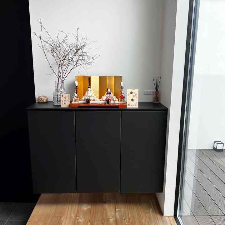 黒いシューズラックが置かれた明るく清潔感のある玄関、木製床とシンプルな飾りでモダンかつナチュラルな雰囲気のインテリア