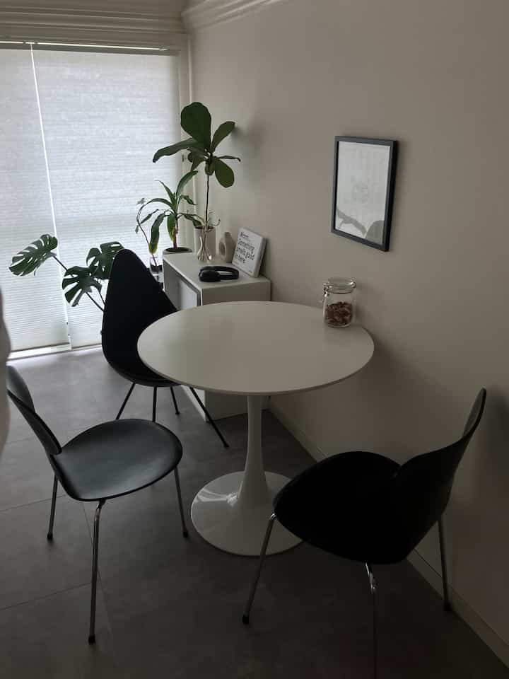 白と黒のトーンのコンパクトなダイニングルーム。丸テーブルと黒いチェア、観葉植物が配置されたミニマルな雰囲気のインテリア