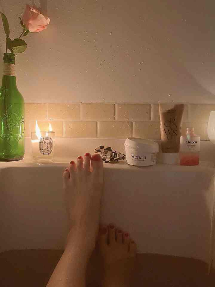 暖かな照明と白いタイルのバスルーム空間、キャンドルと浴槽が配置されており、落ち着いた雰囲気のインテリア