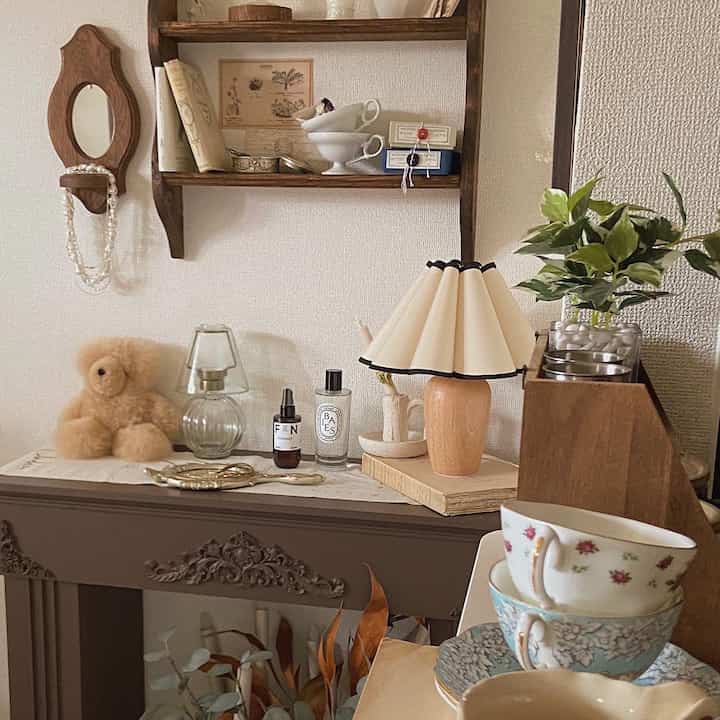Beige and brown toned vintage style living corner featuring wooden shelves, table lamp, and floral patterned teacups in a cozy setting